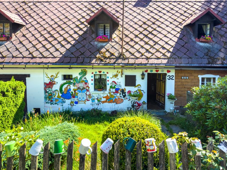 Small painted cottage with a colourful mural and front yard flowers.